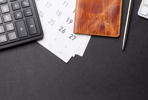 calculator, passport, keyboard, model airplane on desk.
