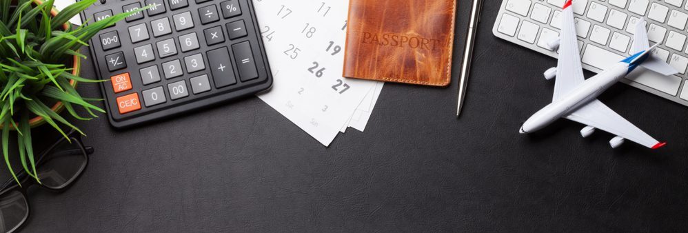 calculator, passport, keyboard, model airplane on desk.