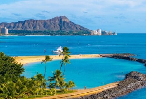 Aerial view of Oahu's Ala Moana Beach park, Waikiki and Diamond Head mountain in distance. blue ocean and palm trees.
