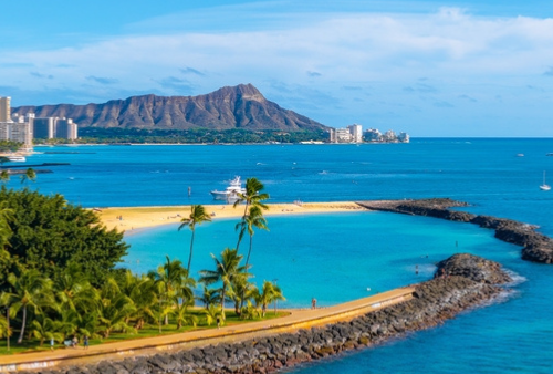 Aerial view of Oahu's Ala Moana Beach park, Waikiki and Diamond Head mountain in distance. blue ocean and palm trees.