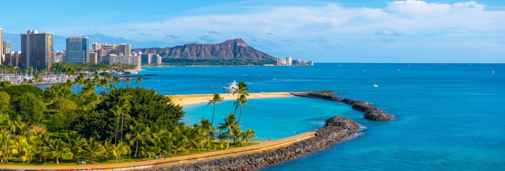 Aerial view of Oahu's Ala Moana Beach park, Waikiki and Diamond Head mountain in distance. blue ocean and palm trees.