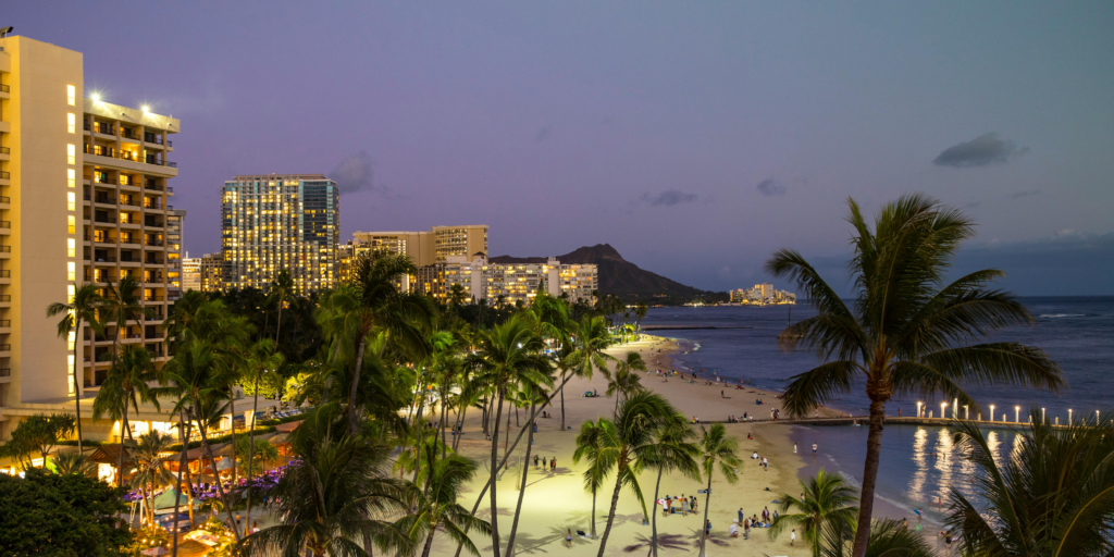 Shoreline of Waikiki Beach at night, palm tress and hotels lights, Diamond Head mountain in backqround