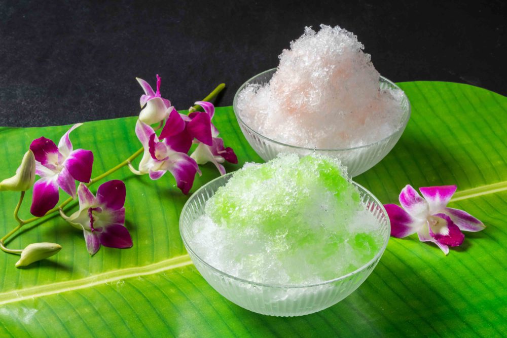 Two bowls of shaved ice placed on palm leaf. surrounded by purple orchids.