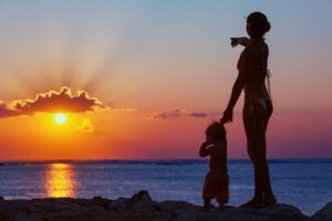 Silhouette of woman and child on beach watching golden sunset.