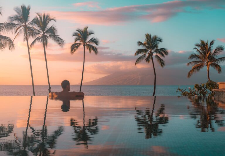 Man sunset silhouette at edge of infinity pool.