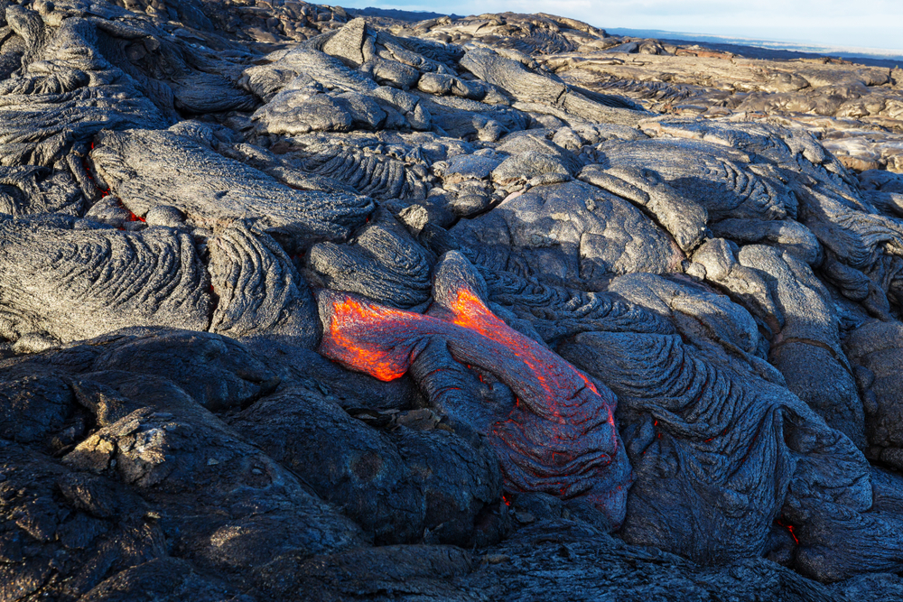 Up close of fresh lava, black with orange glow beneath.