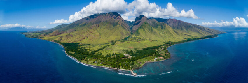 High aerial Shot of Maui. Green mountains, blue ocean on both sides.